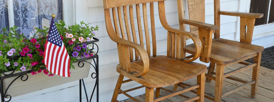 Two wooden chairs on old front porch with flowers and American flag